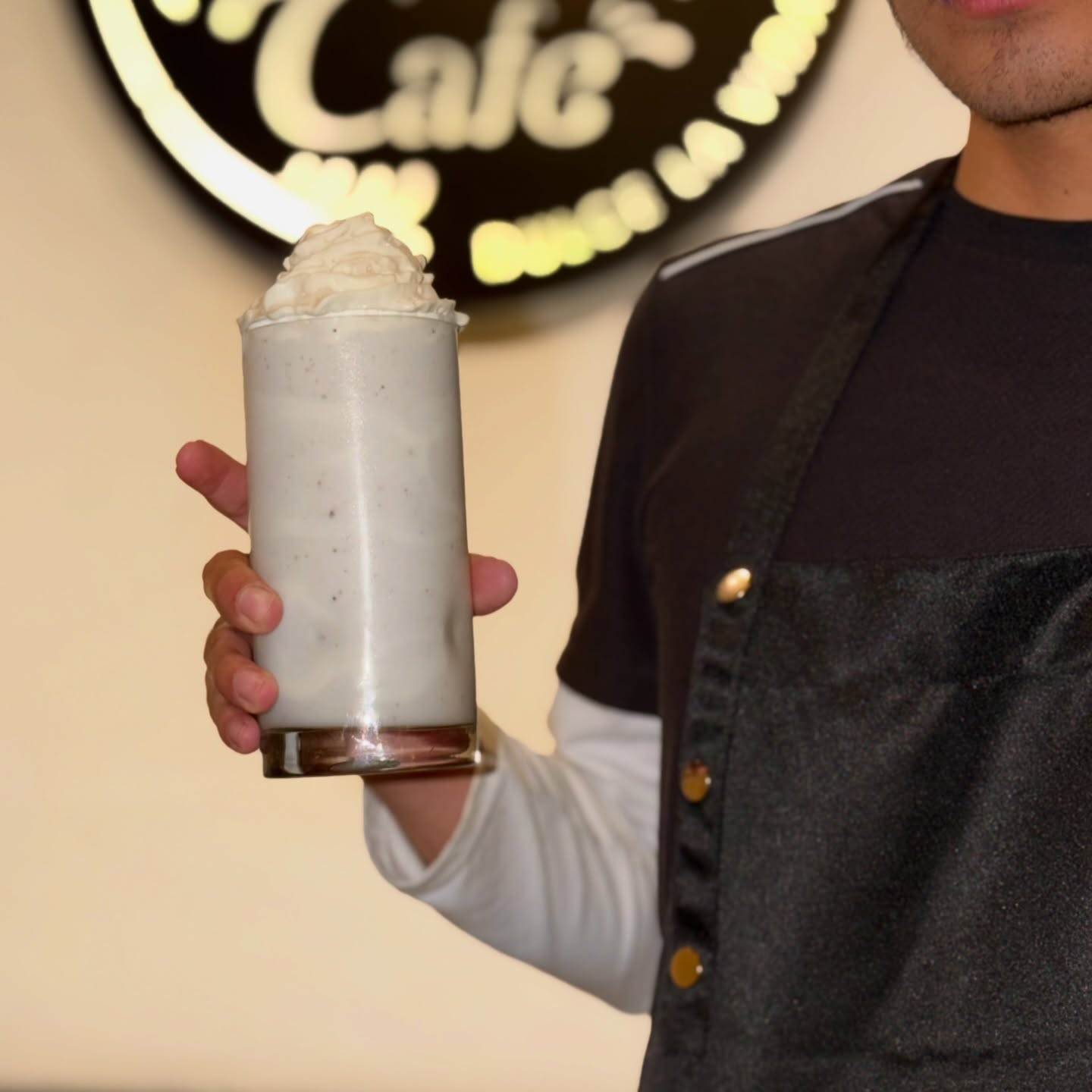 Barista de Amargo El Café sosteniendo un smoothie frente al logo iluminado